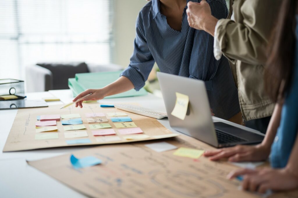 Three people working through a business process mapped out on paper with sticky notes during a scoping session.