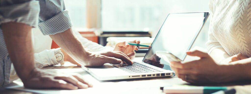 Two people at a desk working together on a laptop and phone, planning social media and search content for a business.