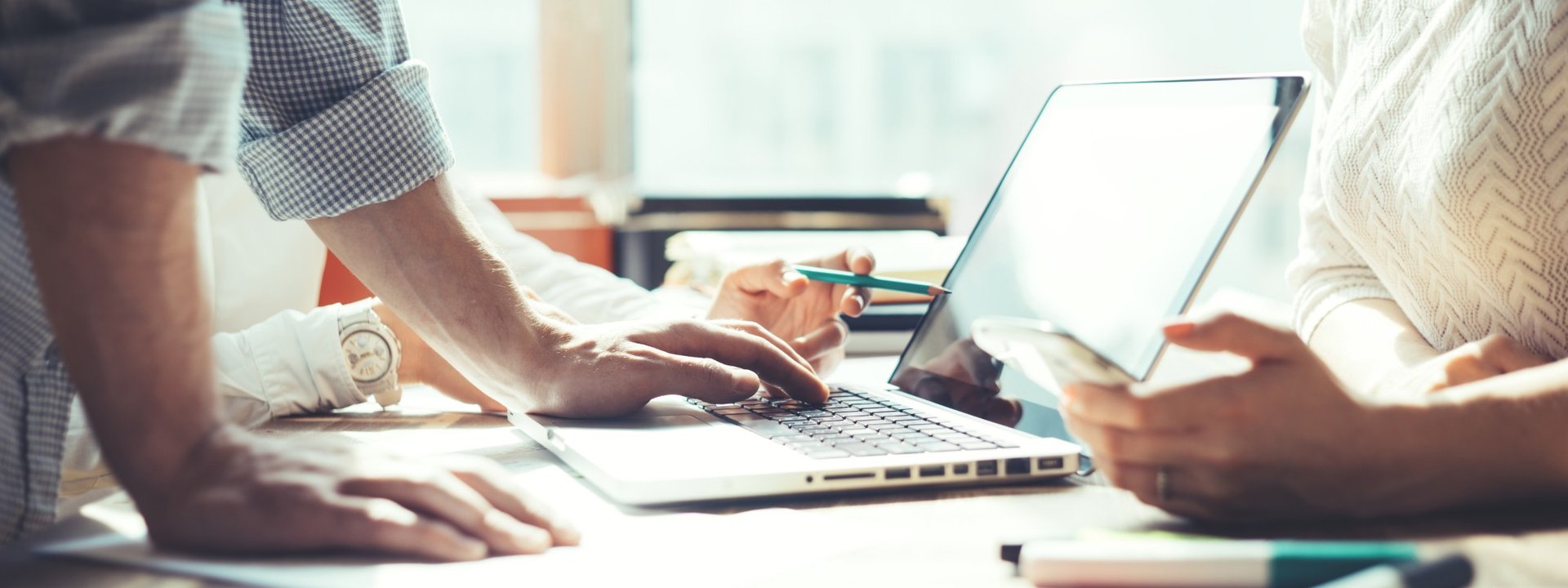 Two people at a desk working together on a laptop and phone, planning social media and search content for a business.